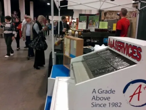 A bustling indoor market scene features a booth with "A+ Services" signage displaying honey products. Shoppers walk by, creating a lively atmosphere.