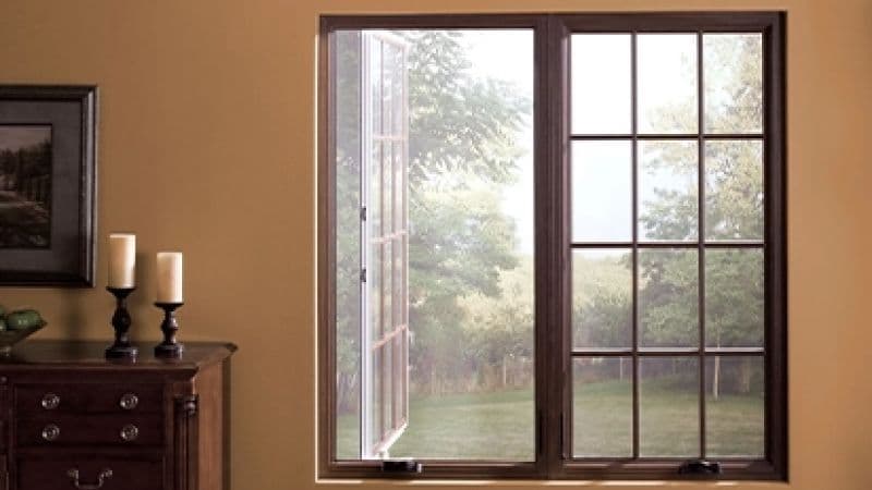 A window looks out onto a bright, serene garden with trees. Indoors, a wooden dresser holds candles, evoking a calm, cozy atmosphere.