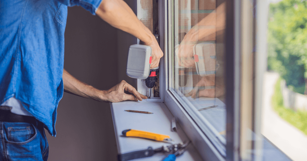 A person installs a window using a power drill, with tools like pliers and a cutter nearby. Sunlight filters through, creating a focused, productive atmosphere.